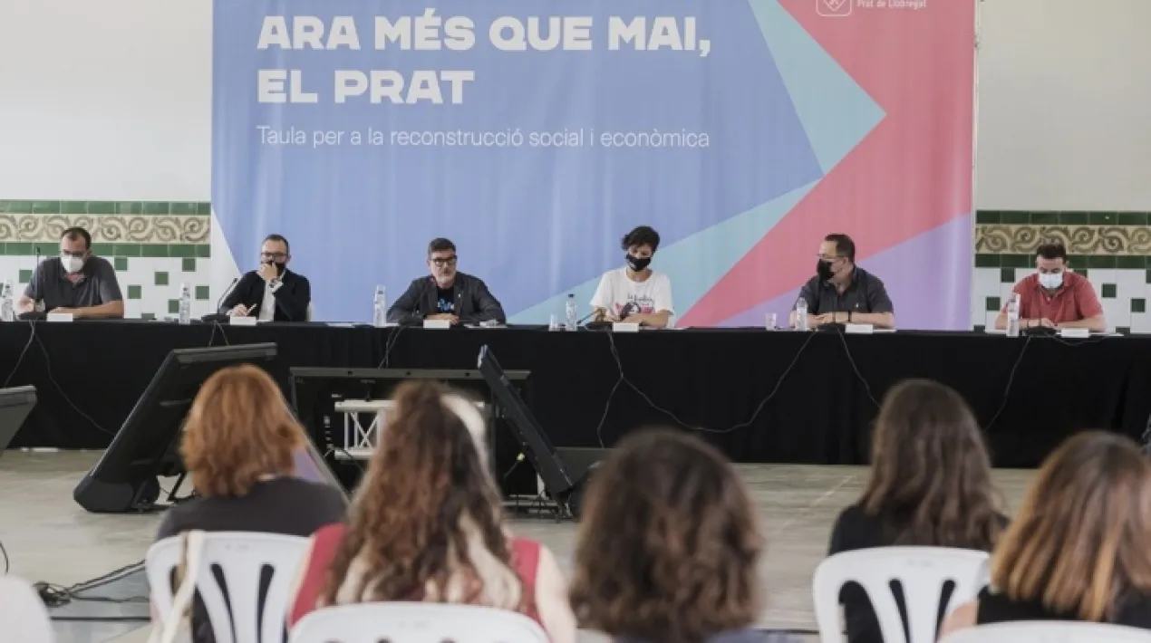  La Granja de la Ricarda ha acollit aquest dimarts, 29 de juny, una reunió de la Taula per a la reconstrucció social i econòmica del Prat. En aquesta trobada, en la qual han participat més d’una vintena de representants dels principals agents socials, polítics i econòmics de la ciutat, s’ha fet balanç de l’estratègia per a la reconstrucció del Prat front a l’impacte de la covid, impulsada ara fa un any, a més de marcar noves mesures per actualitzar-la i adequar-la a l’evolució del context de la pandèmia des de l’estiu de 2020. En la reunió, l’Ajuntament va anunciar que mobilitzarà 8 milions extra més per a l’estratègia de reconstrucció del Prat front a l’impacte socioeconòmic de la pandèmia. S’afegeixen als 6 milions d’euros que ja va invertir l’any passat, arribant a un total de 14 milions d’euros per a l’estratègia de reconstrucció.  L’estratègia de  reconstrucció “Ara més que mai, el Prat” consta de quatre eixos d’actuació específics, amb els objectius generals següents: en primer lloc, promoure una ciutat cohesionada i que cuida, amb mesures per combatre la pobresa i garantir la igualtat en matèria de salut, educació o cultura; en segon lloc, fomentar una ciutat pròspera i activa, amb mesures de suport al teixit comercial, productiu i empresarial; en tercer lloc, potenciar una ciutat resilient i sostenible, amb actuacions adreçades a fomentar les energies renovables, el transport sostenible o l’eficiència energètica; i, en quart lloc, fomentar la innovació, la digitalització i la transparència de l’administració local. De forma transversal, l’Ajuntament també es planteja un model d’atenció que sigui cada vegada més proper a la ciutadania. El nivell d’execució global de l’estratègia de reconstrucció fins al moment és del 76%, percentatge que arriba al 91% en el cas del segon eix d’actuació, adreçat a promoure el teixit comercial, productiu i econòmic. Així ho van exposar les directores de Desenvolupament Econòmic i Acció Social de l’Ajuntament, Esther Pujol i Laia Ortiz, respectivament, que van presentar el balanç del desenvolupament de l’estratègia de reconstrucció fins al moment, a més de presentaran propostes d’acció futures. L’alcalde del Prat, Lluís Mijoler, va presentar l’acte, en què, a partir de l’exposició inicial, es va obrir un debat amb els agents socioeconòmic i polítics de la ciutat integrants de la taula. La salut mental, entre les principals prioritats a partir d’ara A partir d’ara, és previst reforçar les mesures d’acompanyament a la salut mental i el benestar emocional. Fins al moment, ja s’havien posat en marxa alguns serveis concrets, com l’Activa’t, que està donant orientació i suport a persones que necessiten ajuda en matèria de salut mental. Però, d’ara en endavant, es reforçaran els serveis d’atenció a la salut mental comunitària, cosa que comportarà el reforç del suport psicològic i el desenvolupament de programes psicoeducatius o de Grups d’Ajuda Mútua. També es promourà la cooperació intermunicipal per la salut mental comunitària amb d’altres municipis com Sant Just Desvern, Sant Boi de Llobregat o Sant Joan Despí. A més, es duran a terme mesures específiques per vetllar pel benestar emocional de les persones joves i de la gent gran, a partir de propostes d’acció comunitària.  D’altra banda, és previst reactivar el proper mes de setembre la prescripció social en matèria de salut, que passa per recomanar la realització de diferents activitats disponibles a la ciutat (de caire esportiu, terapèutic, cultural...) per millorar diferents vessants de la salut (física o mental). Protegir els espais naturals front a l’amenaça que suposa el projecte d’ampliació de l’aeroport i promoure la transició energètica L’actualització de l’estratègia de reconstrucció també emfasitza la necessitat de preservar i protegir els espais naturals i protegits i el Parc Agrari del Baix Llobregat, definint una estratègia política i jurídica amb aquest objectiu, i més encara davant de l’amenaça per a l’equilibri territorial que suposen propostes com la de l’ampliació de l’aeroport. També se seguirà desplegant l’estratègia de transició energètica al Prat. Així per exemple, a partir del curs 2021-2022 s’iniciarà una prova pilot per començar a aportar energia d’origen fotovoltaic i de proximitat a partir de les AMPAs de les escoles. Servirà com a prova pilot per a la futura posada en marxa de les plaques d’energia fotovoltaica en 22 teulades d’equipaments municipals (amb 1 MWp total d’energia). Garantir el dret a l’habitatge i prevenir l’exclusió residencial Així mateix, s’impulsaran diverses mesures per garantir el dret a l’habitatge digne. Diversos dels objectius de l’estratègia de reconstrucció estan alineats amb el Pla local d’habitatge 2021-2027, que preveu doblar els pisos de lloguer social i assequible a la ciutat en aquest període, passant dels 329 actuals a més de 600 . L’estratègia de reconstrucció també reforça les mesures contra el sensellarisme. Per exemple, s’iniciarà el primer programa Housing First, que passa per proporcionar un habitatge a les persones sense llar com a primer pas per fomentar la seva inclusió sociolaboral. S’ampliaran els pisos d’inclusió i els serveis per atendre aquest col·lectiu. La reactivació del comerç i l’ocupació A més, es portaran a terme noves mesures de suport al teixit comercial de la ciutat. Així per exemple, es desenvoluparà un pla de dinamització de locals buits, per potenciar la seva recuperació i la seva adequació per instal·lar-hi noves activitats productives i comercials. També s’impulsarà el pla de millora de la sostenibilitat, perquè l’activitat comercial pugui emprendre mesures adreçades a l’eficiència i estalvi energètic. Pel que fa a la inserció sociolaboral, es reforçaran els programes per donar suport a les persones que han vist afectada la seva situació ocupacional en el context de la pandèmia. La reactivació de la pràctica cultural, esportiva i associativa Des d’aquest estiu, també es començarà a impulsar un pla de reactivació de l’activitat cultural, així com de dinamització del teixit associatiu i d’entitats de la ciutat, que s’ha vist fortament afectat pel context de la pandèmia. A més, es posaran en marxa diverses mesures per promoure la reactivació de la pràctica esportiva entre la ciutadania, amb mesures específiques per a infants i joves. Balanç de les mesures desenvolupades fins ara En l’àmbit d’acció social, cal destacar la posada en marxa de l’OIAS (Oficina Integral d’Atenció Social) el maig de 2020, per tal de fer front a l’augment de necessitats socials (alimentàries i bàsiques, ajuts en la gestió de prestacions, etc.) derivades de la pandèmia i centralitzar en una finestreta única d’atenció les diferents sol·licituds de la ciutadania en aquesta matèria.  Així mateix, cal destacar que s’ha iniciat la  revisió i reforma del model de cures a la gent gran. S’està impulsat un nou model de Servei d’Atenció domiciliària, que millora la qualitat del servei, diversificant-lo i potenciant illes socials de cures amb equips de professionals qualificats que treballen des de la proximitat amb la comunitat. En l’àmbit de l’educació, s’han impulsat mesures per combatre l’escletxa digital entre l’alumnat, per exemple el repartiment de tauletes tàctils a infants sense ordinador o accés a Internet a la seva llar. També s’ha impulsat la digitalització en la pròpia administració municipal, facilitant els tràmits online o el servei de cita prèvia, i també s’ha contribuït a dinamitzar el comerç online. Pel que fa a l’economia local, cal destacar la bateria d’ajuts al comerç per tornar a aixecar la persiana després de mesos de tancament i per al manteniment de la seva activitat. Finalment, en matèria de sostenibilitat, cal recordar que el setembre de 2020 el ple municipal va aprovar la Declaració d’emergència climàtica del Prat, que va suposar l’inici de l’estratègia de transició energètica de la ciutat. Entre les principals mesures iniciades fins ara, destaquen l’obertura de la Casa de l’Energia, per oferir assessorament en aquesta matèria el gener de 2021.Veure més